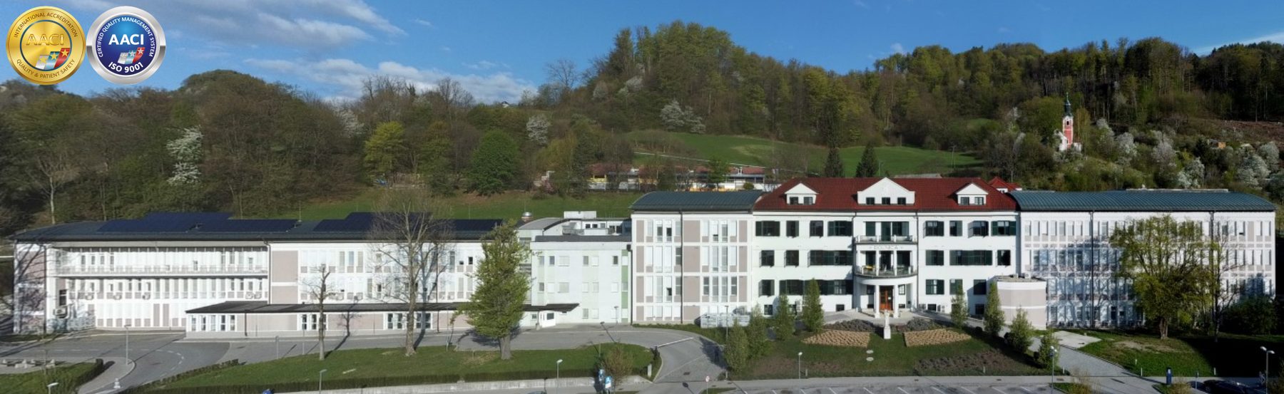 Pogled iz zraka na kompleks Splošne bolnišnice Trbovlje ob gozdnatem pobočju