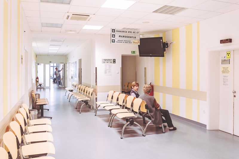 Hodnik specialističnih ambulant s čakalnimi stoli in oznakami ambulant.